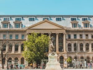 Front view of a historic university building with a prominent statue under a clear sky.
